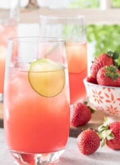 Three glasses of watermelon agua fresca on a table in front of a window with white window panes.