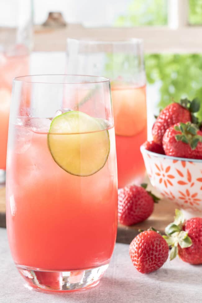 Three glasses of watermelon agua fresca on a table in front of a window with white window panes.