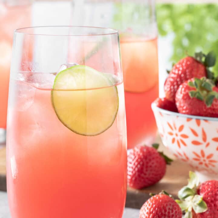 Three glasses of watermelon agua fresca on a table in front of a window with white window panes.