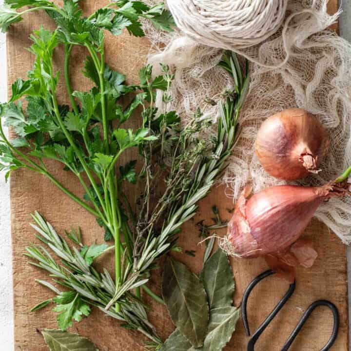 Fresh parsley, thyme and rosemary on a wood cutting board next to a ball of string and small scissors.