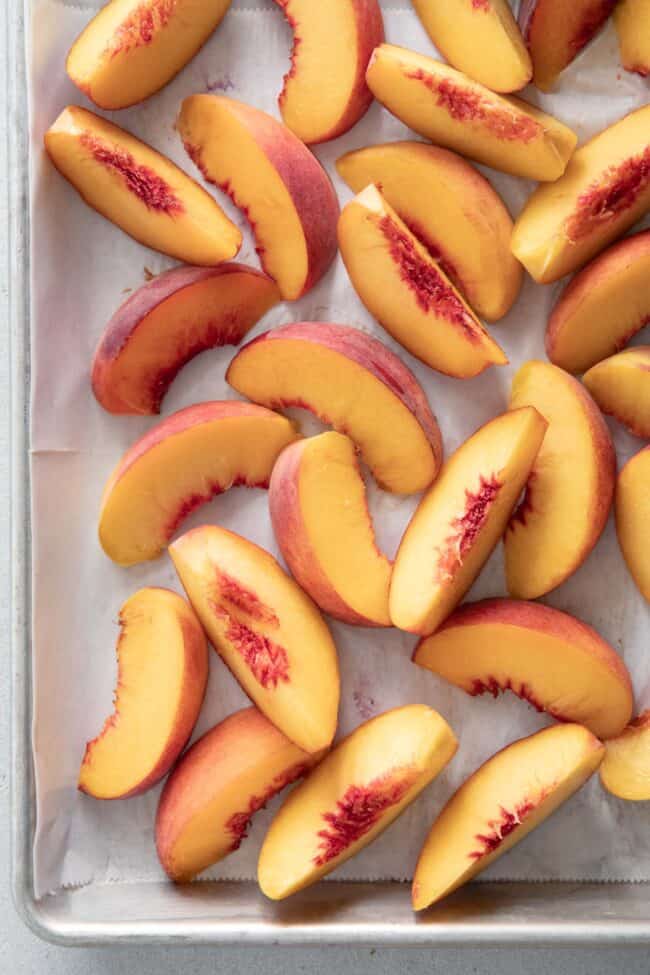 Many slices of stone fruit scattered on a cookie sheet.