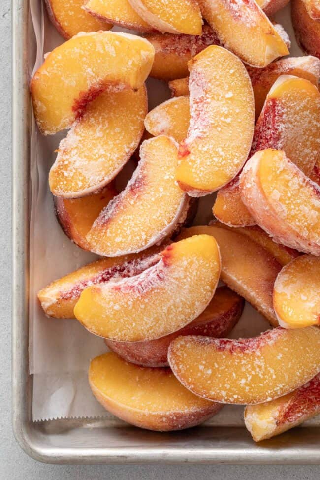 Many frozen peaches piled on a cookie sheet for How to Freeze Peaches.