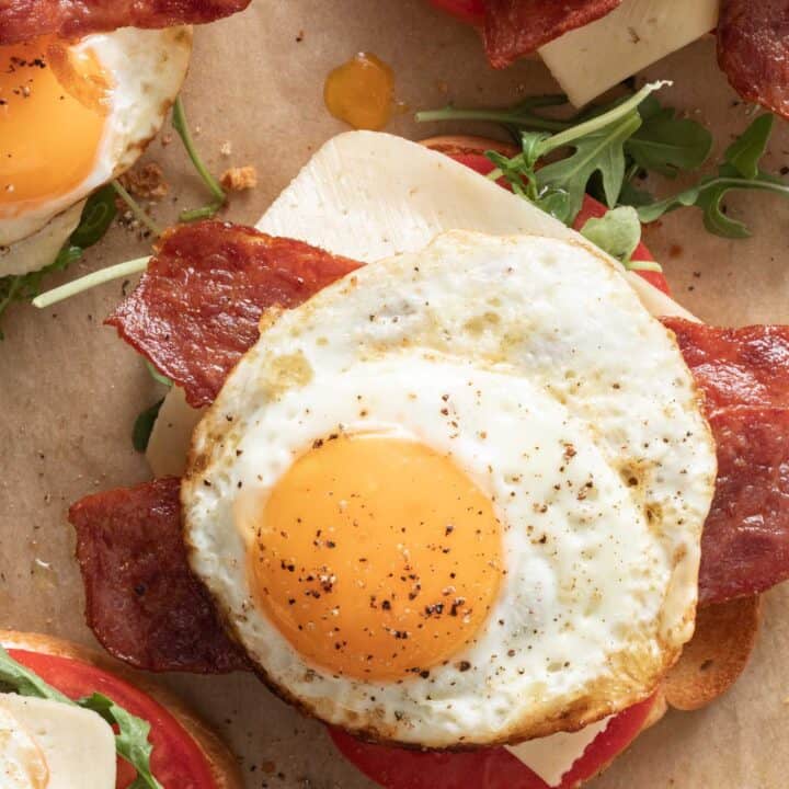 A fried egg sandwich with eggs, turkey bacon, cheese, arugula and tomato on a piece of parchment paper.