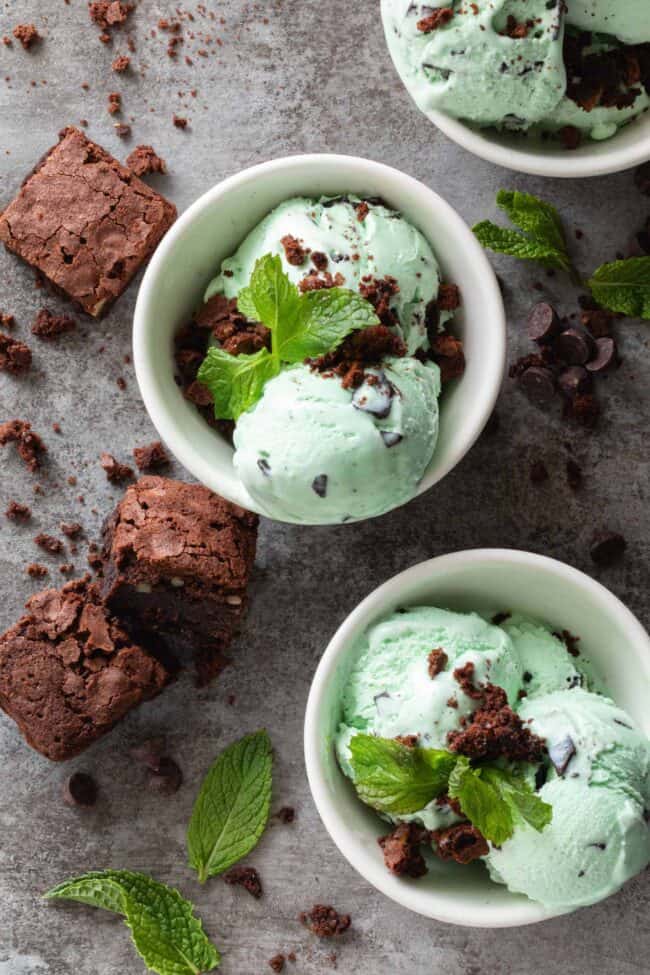 Three small white bowls filled with mint chocolate chip ice cream with brownies crumbled on top.