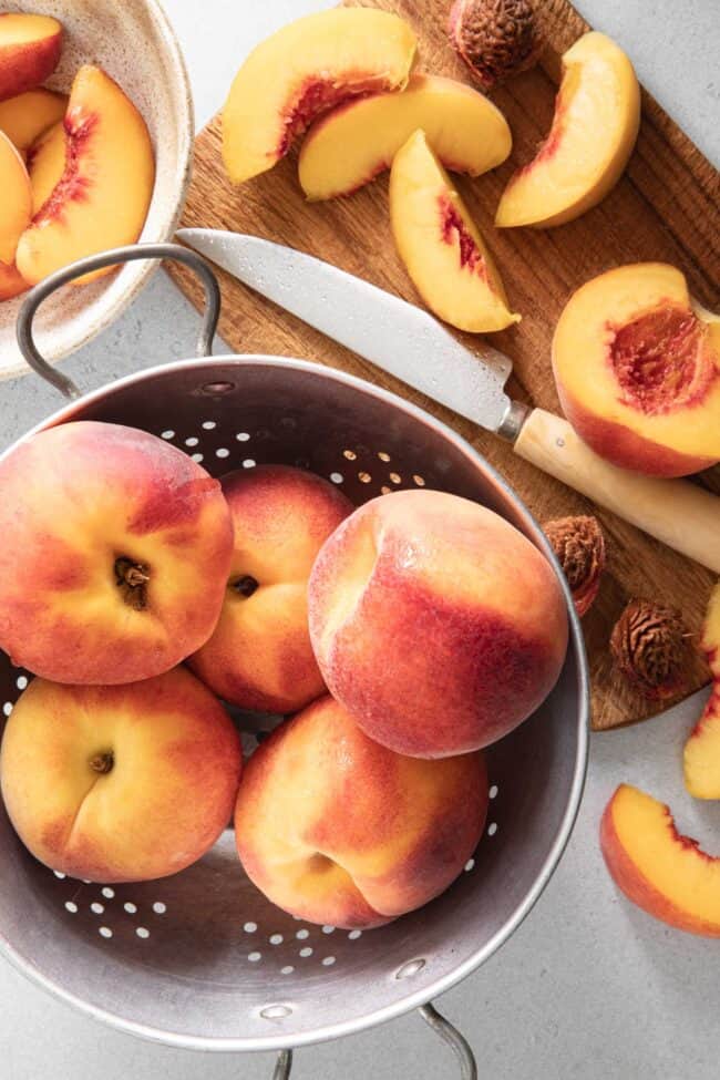 A colander filled with stone fruit sits next to a cutting board with cut stone fruit.