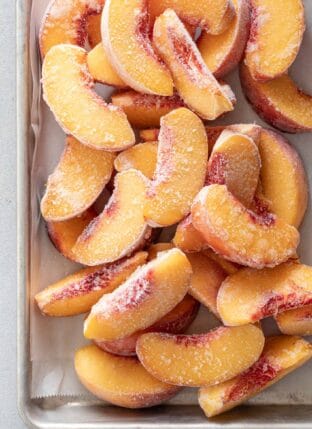 Many frozen peaches piled on a cookie sheet for How to Freeze Peaches.