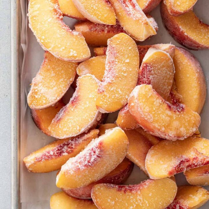 Many frozen peaches piled on a cookie sheet for How to Freeze Peaches.