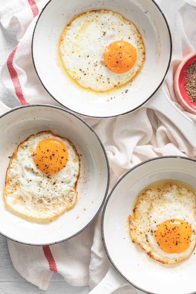 Three small white pans each filled with a fried egg.