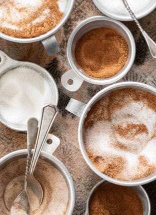 Aluminum measuring cups filled with cinnamon and sugar.