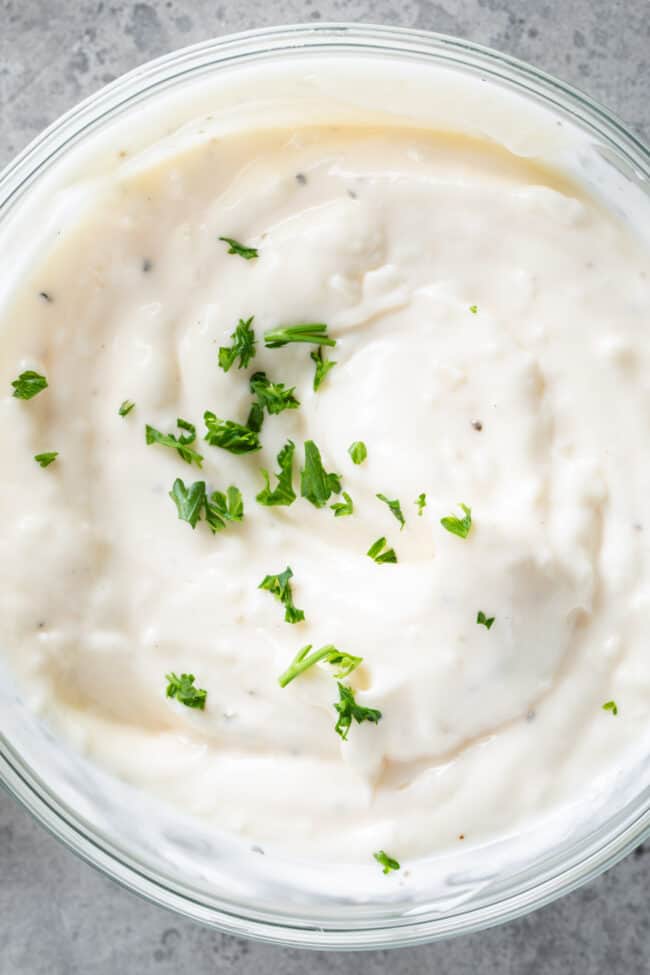 A clear glass bowl filled with mayonnaise and sprinkled chopped parsley on top.