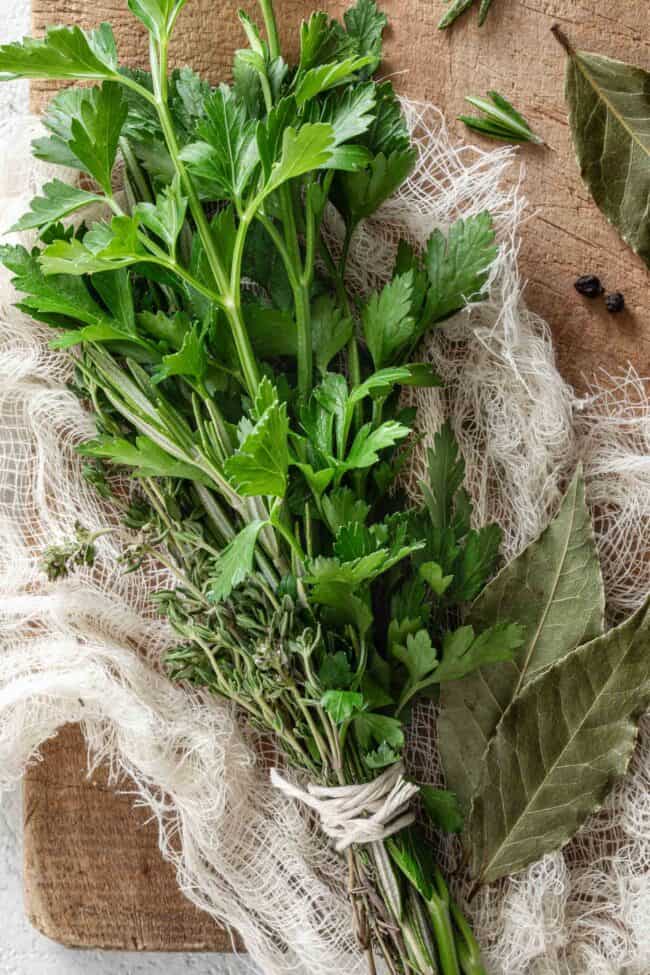 A bundle of fresh parsley, thyme and rosemary (bouquet garni) are tied together on a wood cutting board.