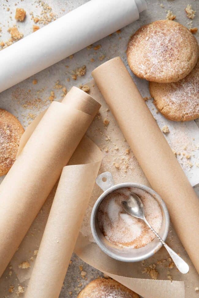 Three rolls of parchment paper scattered on a surface with cookies and crumbs.