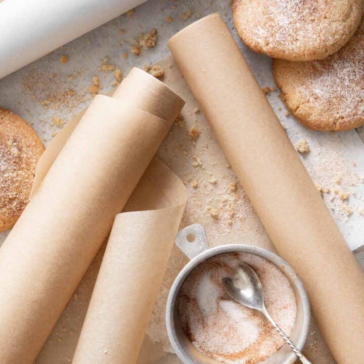 Three rolls of parchment paper scattered on a tray with cookies next to them.