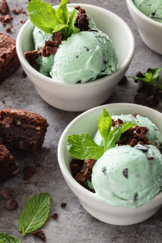 Three small white bowls filled with mint chocolate chip ice cream with brownies crumbled on top.