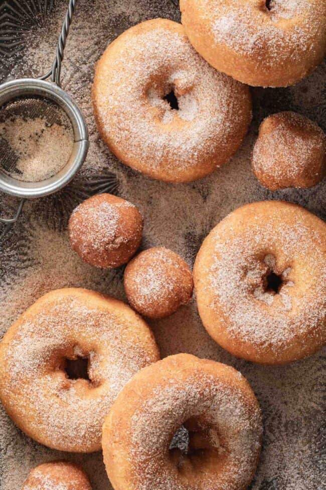 Plain donuts on a cookie sheet dusted with cinnamon sugar