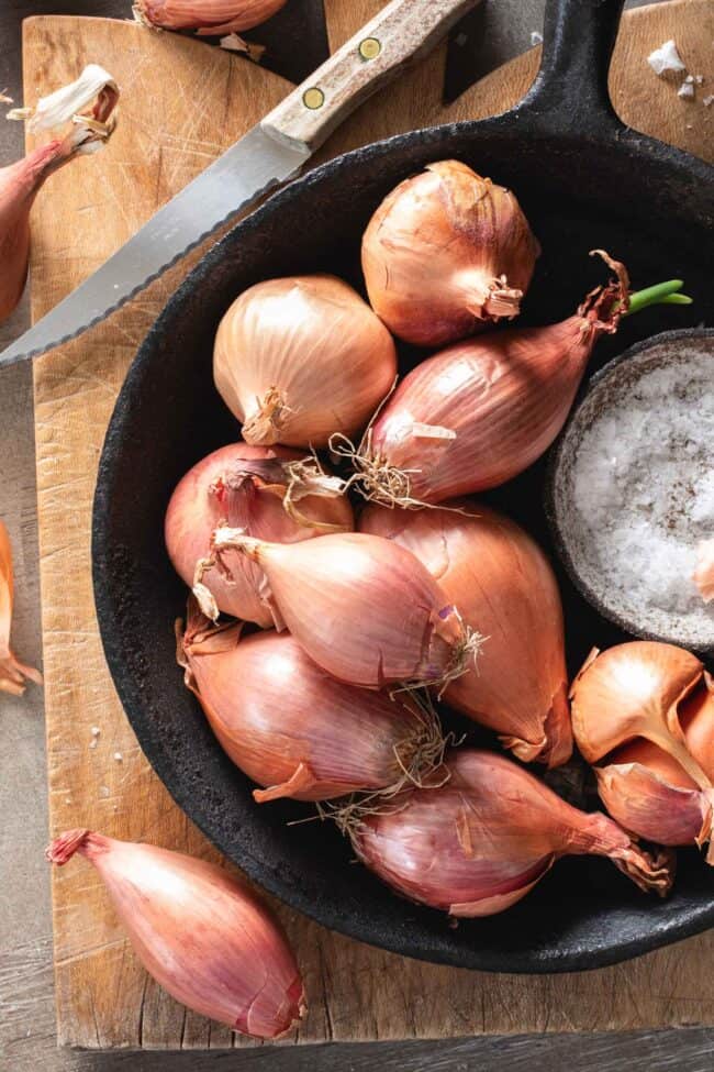 A small cast iron pan filled with shallots. A knife sits next to the pan.