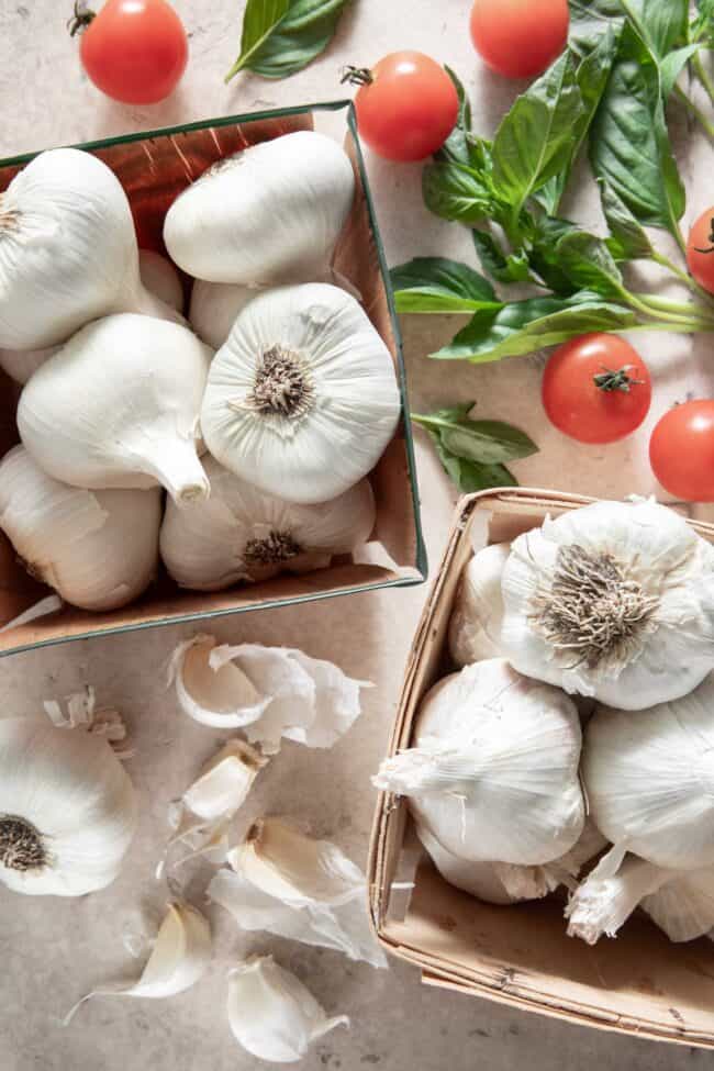 Two wooden baskets filled with whole heads of garlic with cloves scattered next to the boxes. (For is garlic a vegetable).