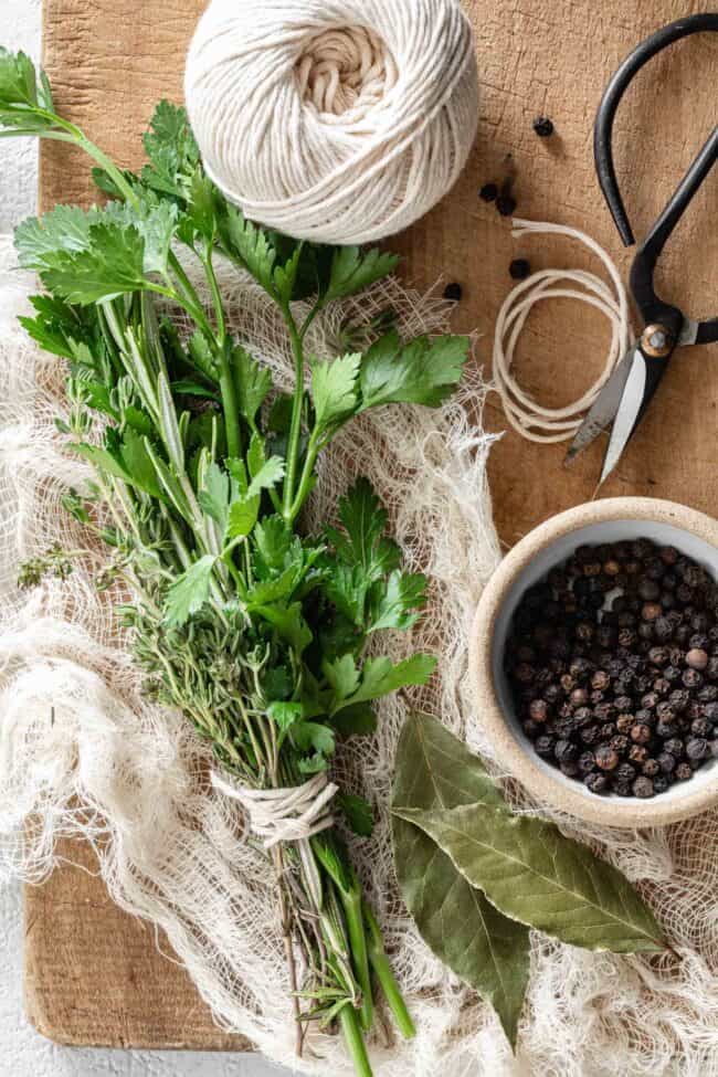 Fresh herbs are tied together with string on a piece of cheesecloth next to a small pair of scissors.