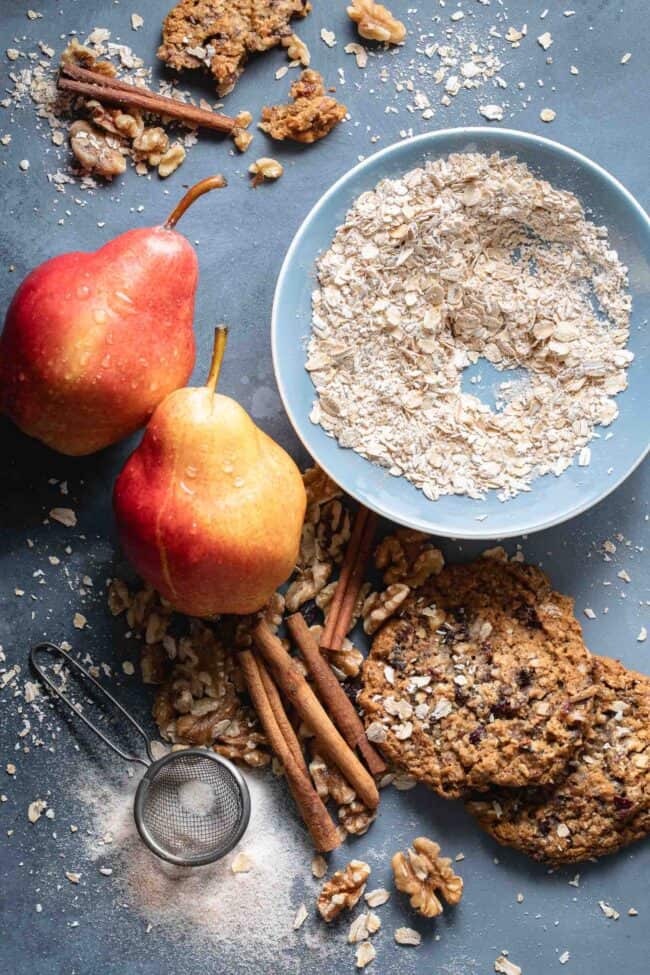 A small blue bowl filled with raw oatmeal next to cinnamon sticks, pears and walnuts.