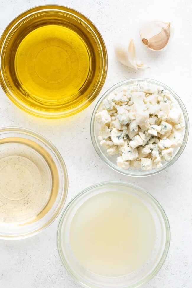 Clear glass bowls filled with olive oil, vinegar, lemon juice and cheese crumbles.