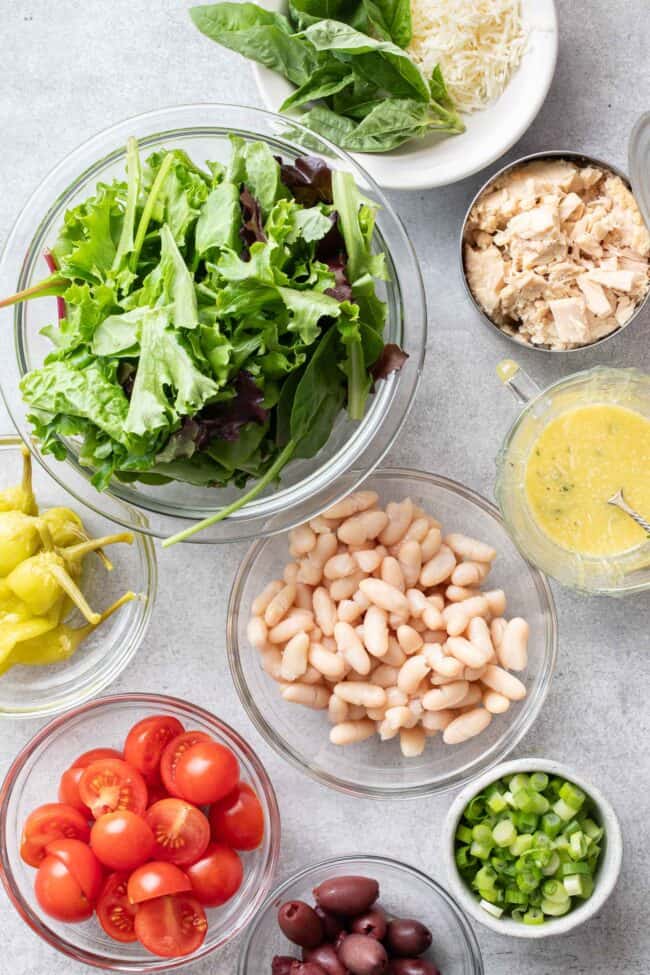 Clear glass bowls filled with lettuce, cannellini beans, cherry tomatoes and kalamata olives.