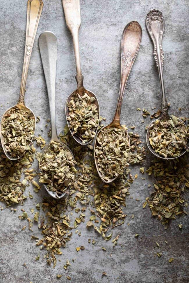 Five spoons filled with dried herbs.