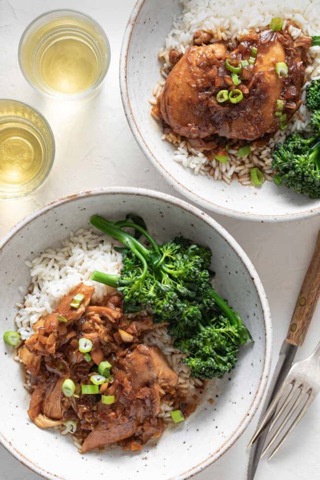 Two white plates filled with Adobo Filipino chicken on a bed of white rice. Steamed broccoli sits next to the chicken.