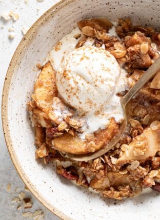 A bowl filled with the best apple crisp with a scoop of vanilla ice cream on top.