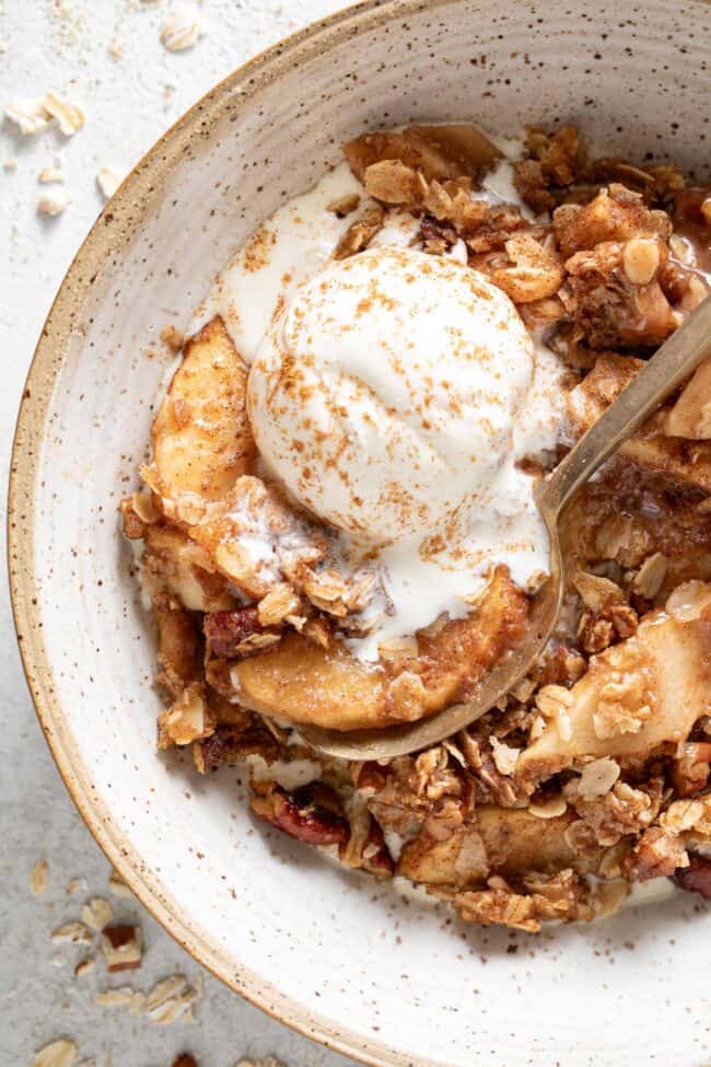 A bowl filled with apple crisp and a scoop of vanilla ice cream.