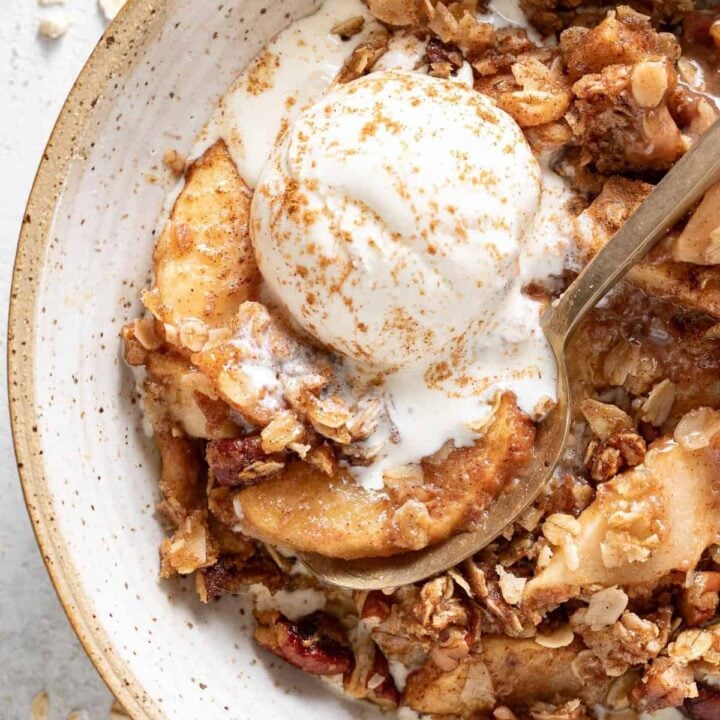 A bowl filled with the best apple crisp with a scoop of vanilla ice cream on top.