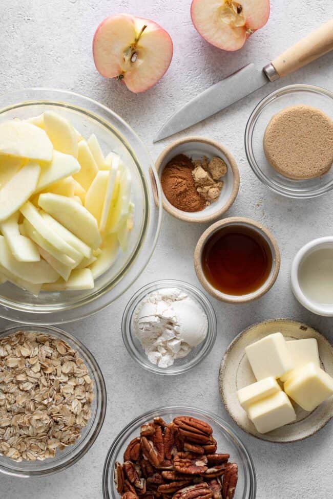 Several small glass bowls filled with spices, oats, sugar, nuts and butter for apple crisp recipe.