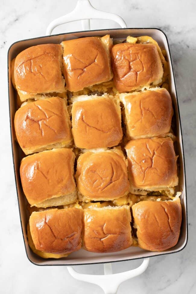 A white baking dish filled with rolls stuffed with scrambled eggs, sausage patties and melted cheese.