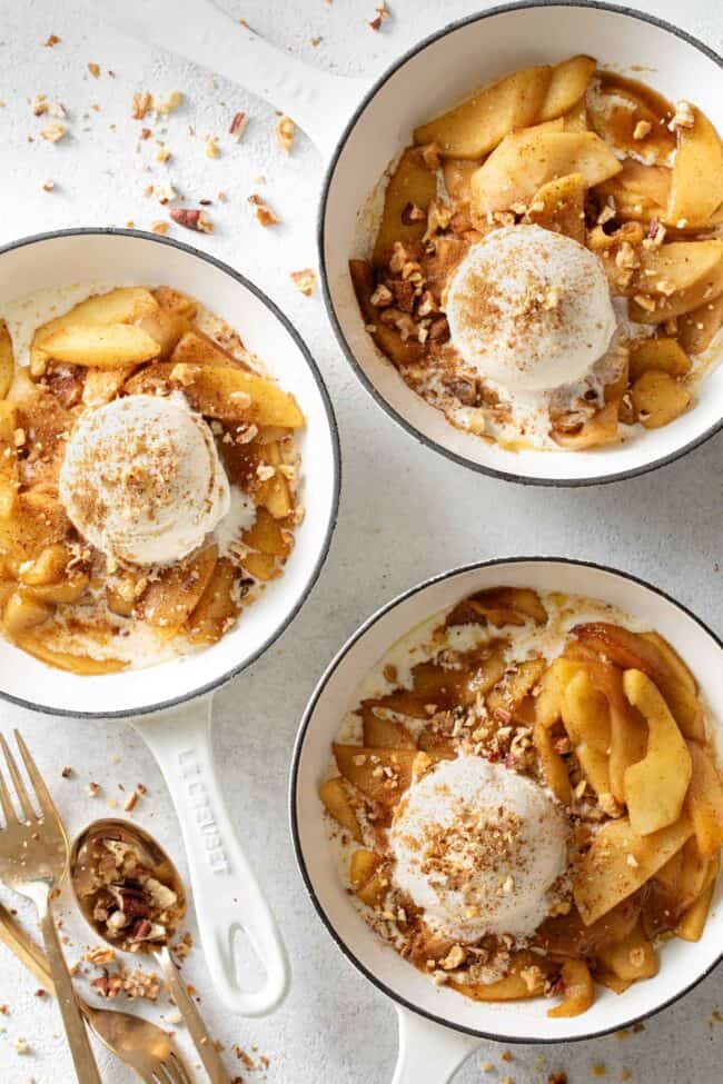 Three white skillets filled with cooked fruit and ice cream.