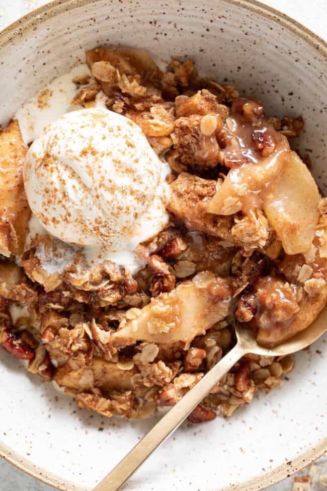 A bowl filled with apple crisp and a scoop of vanilla ice cream on top.