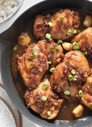 A white skillet filled with 6 pieces of Filipino Adobo simmering in sauce.