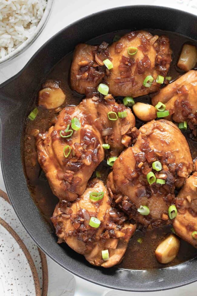 A white skillet filled with 6 pieces of Filipino Adobo simmering in sauce.