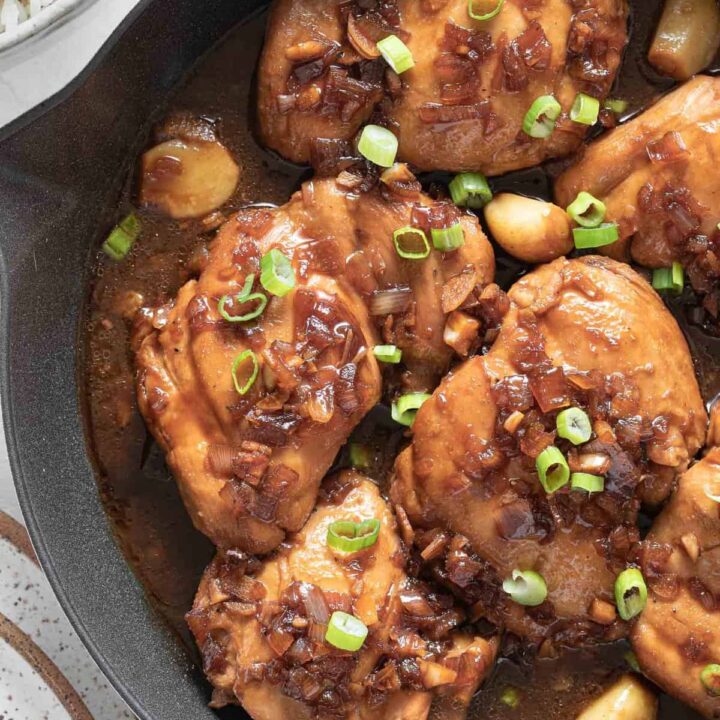 A white skillet filled with 6 pieces of Filipino Adobo simmering in sauce.