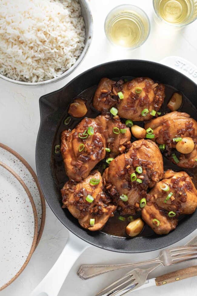 A white skillet filled with six pieces of simmered adobo Filipino chicken.