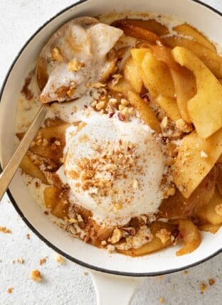 A white skillet filled with fried apples and a scoop of vanilla ice cream.