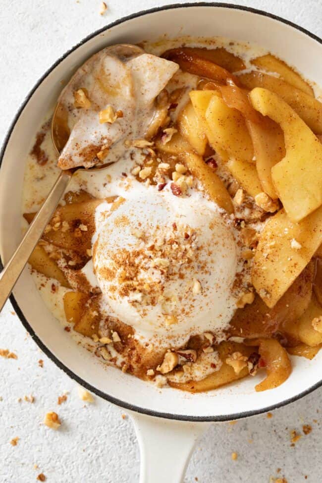 A white skillet filled with fried apples and a scoop of vanilla ice cream.