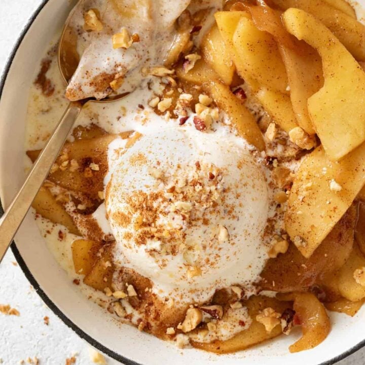 A white skillet filled with fried apples and a scoop of vanilla ice cream.