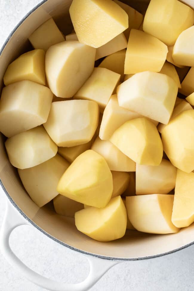 A white pot filled with peeled and cut vegetables.