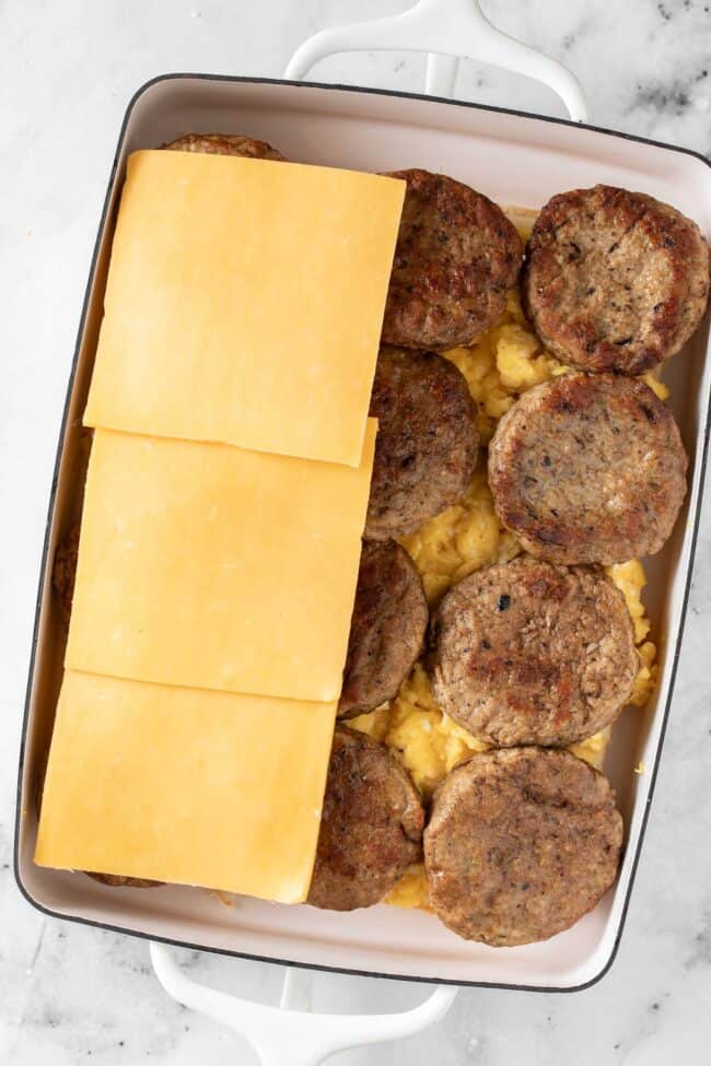 A white baking dish filled with scrambled eggs, sausage patties and cheddar cheese slices.