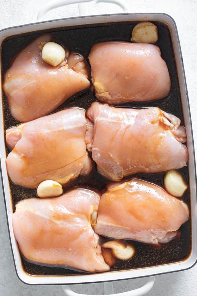Six raw chicken breasts marinate in a white baking pan.