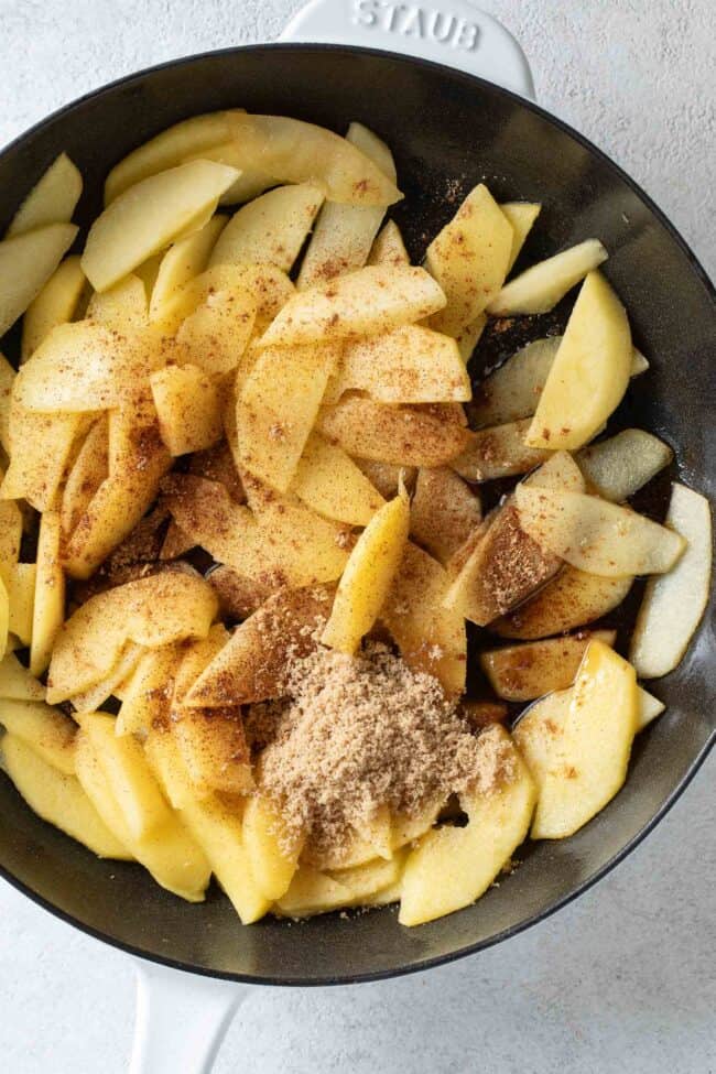 A black skillet filled with sliced fruit with cinnamon and sugar.