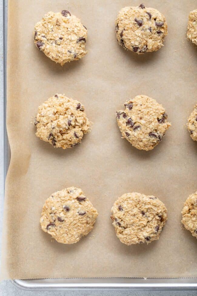 Raw cookie batter scoops on a parchment lined cookie sheet.