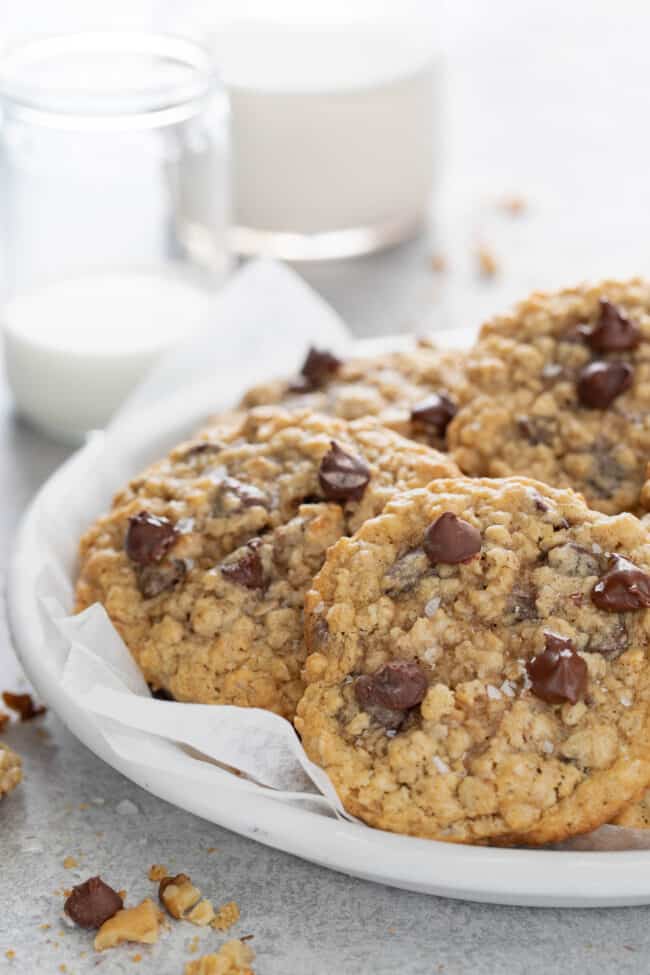 Oatmeal chocolate chip cookies on a white plate with two glasses of milk next to it.