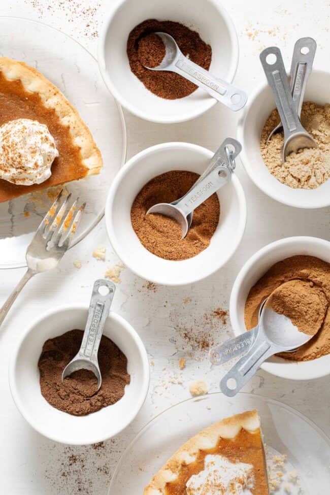 Five small white bowls filled with spices for homemade Pumpkin Pie Spice recipe.