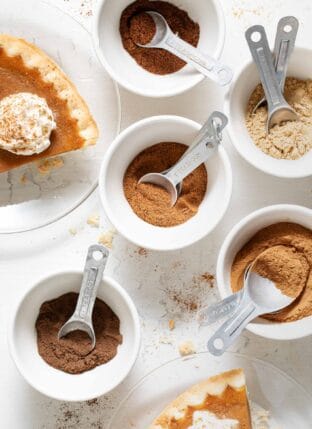 Five small white bowls filled with spices to make pumpkin pie spice substitute.