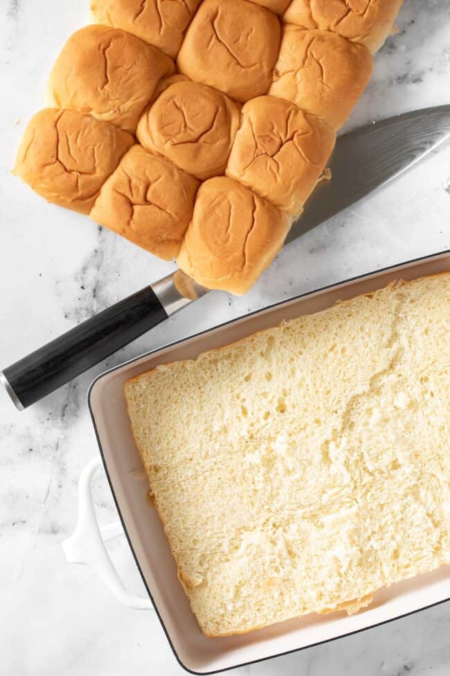 A package of rolls sliced in half sits on a counter next to a sharp knife.